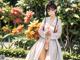 A woman in a white kimono standing in front of flowers.