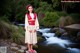 A woman in a red and white kimono standing by a stream.