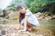 A young girl in a blue and white dress crouching on a rocky beach.