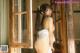 A woman in a white lingerie standing in front of a window.