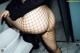 A woman in fishnet stockings is sitting on a toilet.